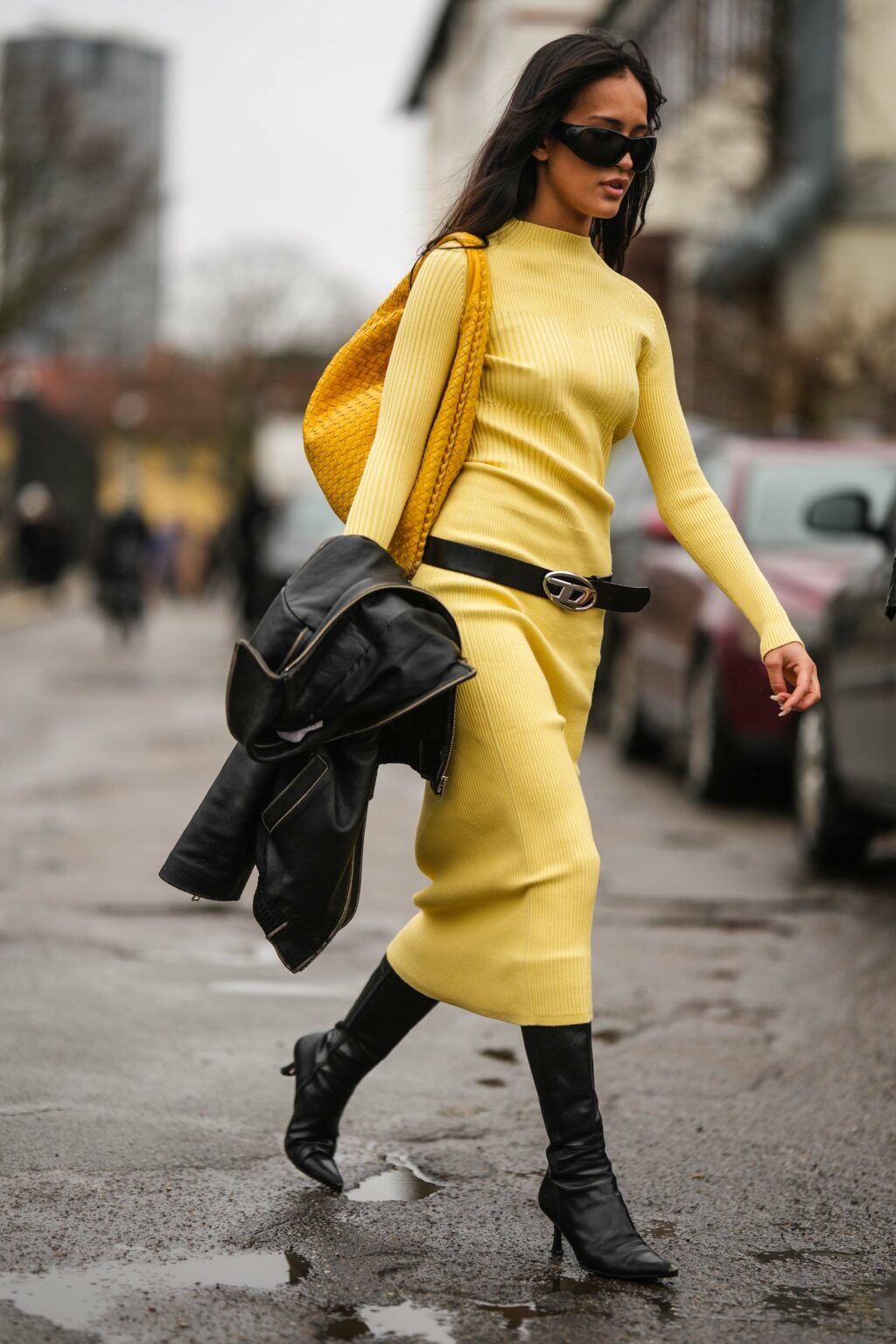 Moteris, dėvinti ilgą geltoną trikotažinę suknelę ilgomis rankovėmis ir juodus ilgaaulius batus