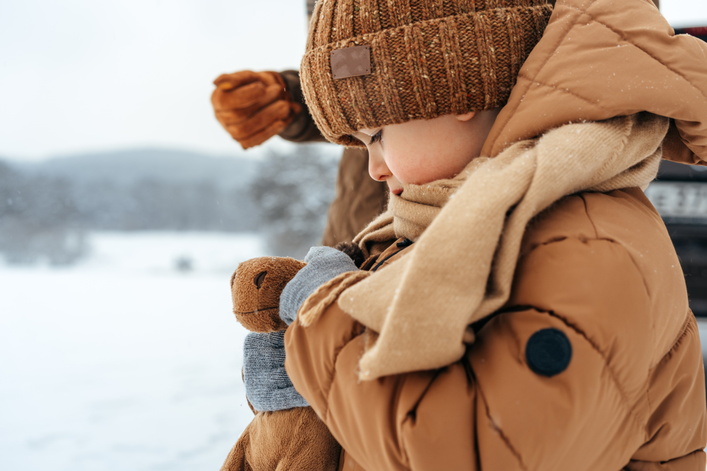 Vaikas, dėvintis rudą žieminę striukę, rudą šaliką ir kepurę